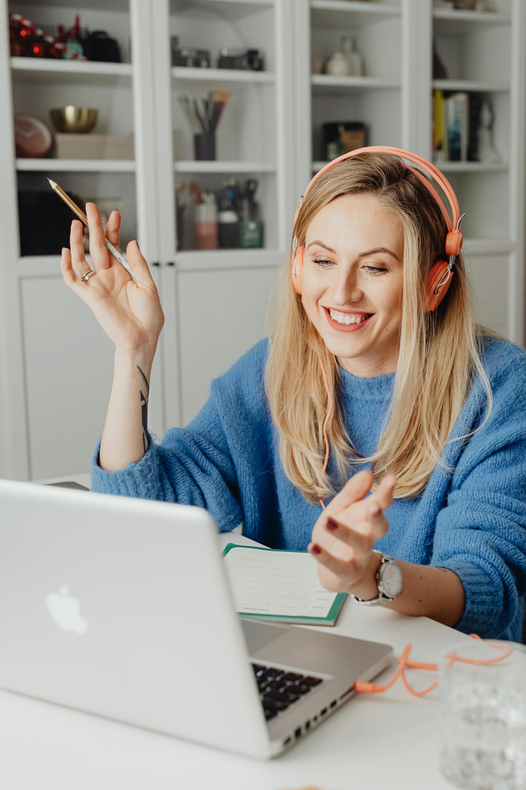 A cheerful woman in a blue sweater video chatting on a laptop at home.
