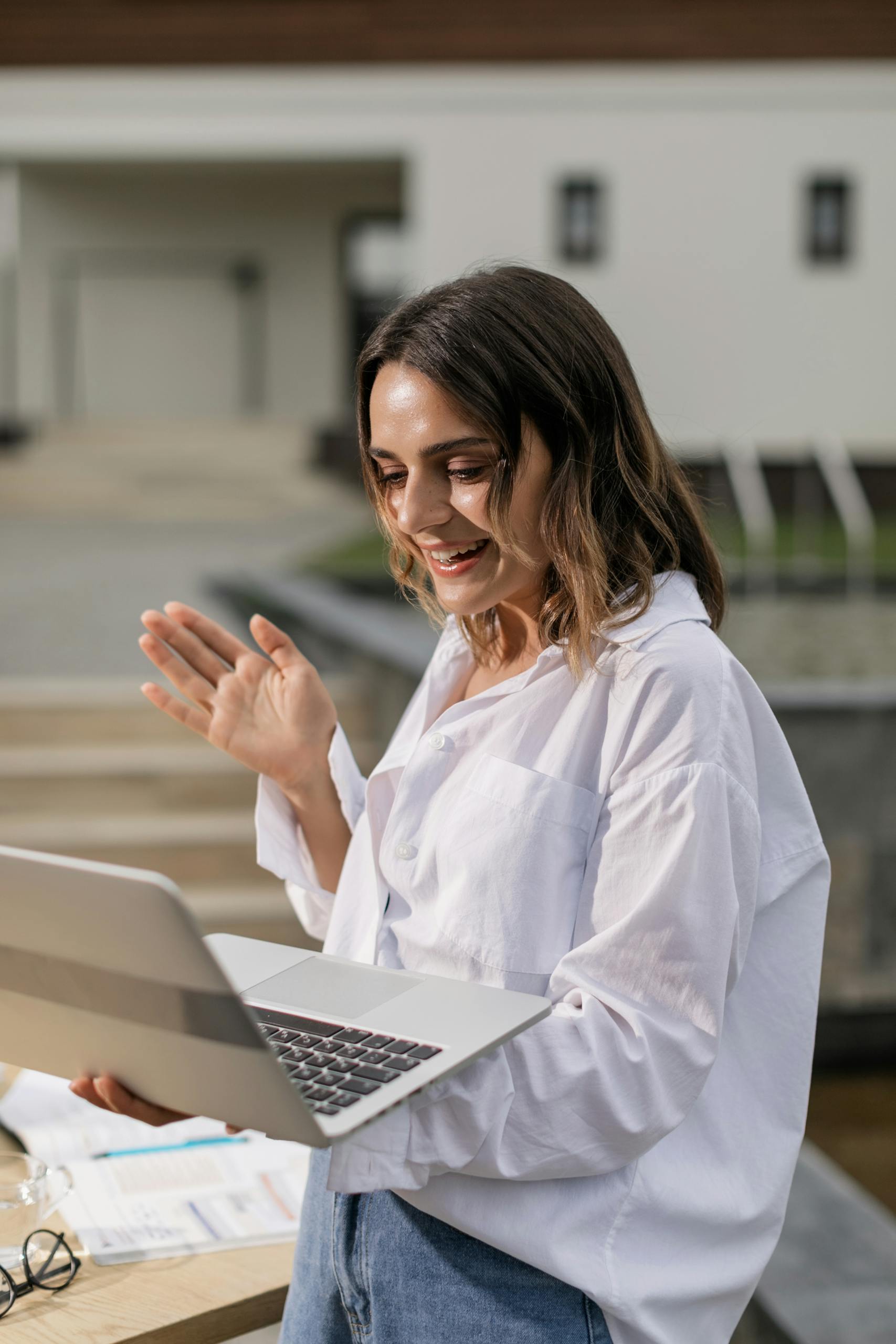 Young woman in white shirt smiling during a video call on her laptop outside.